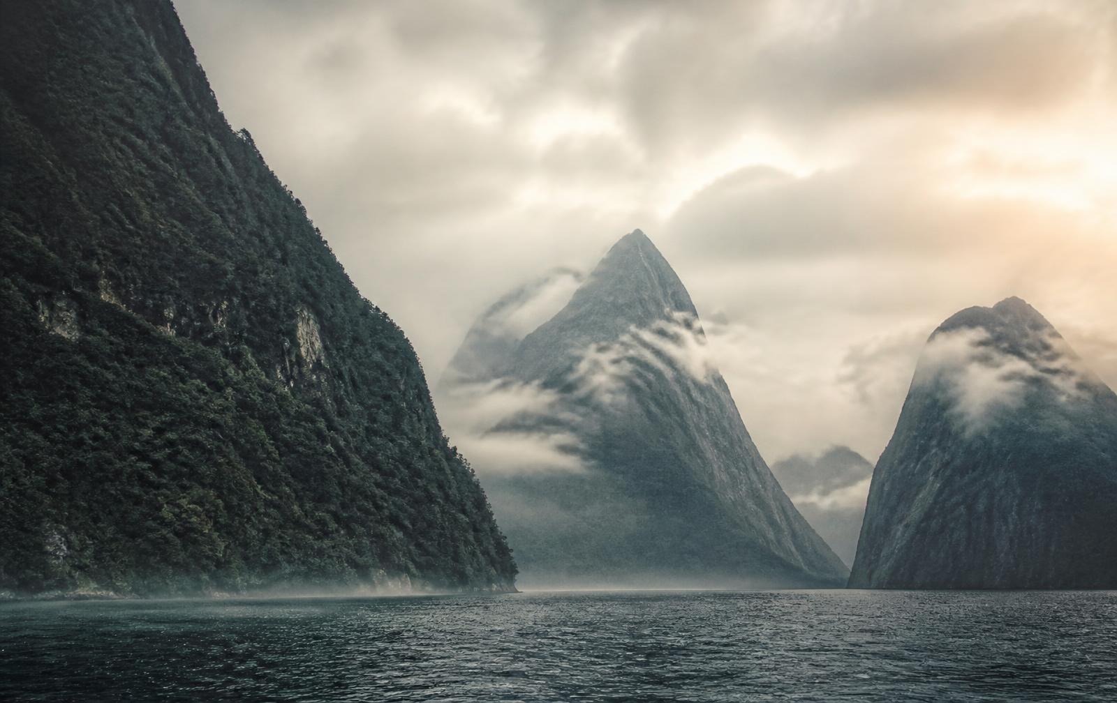 Mist over a New Zealand fiord at dawn, steep forested cliffs rising from dark water