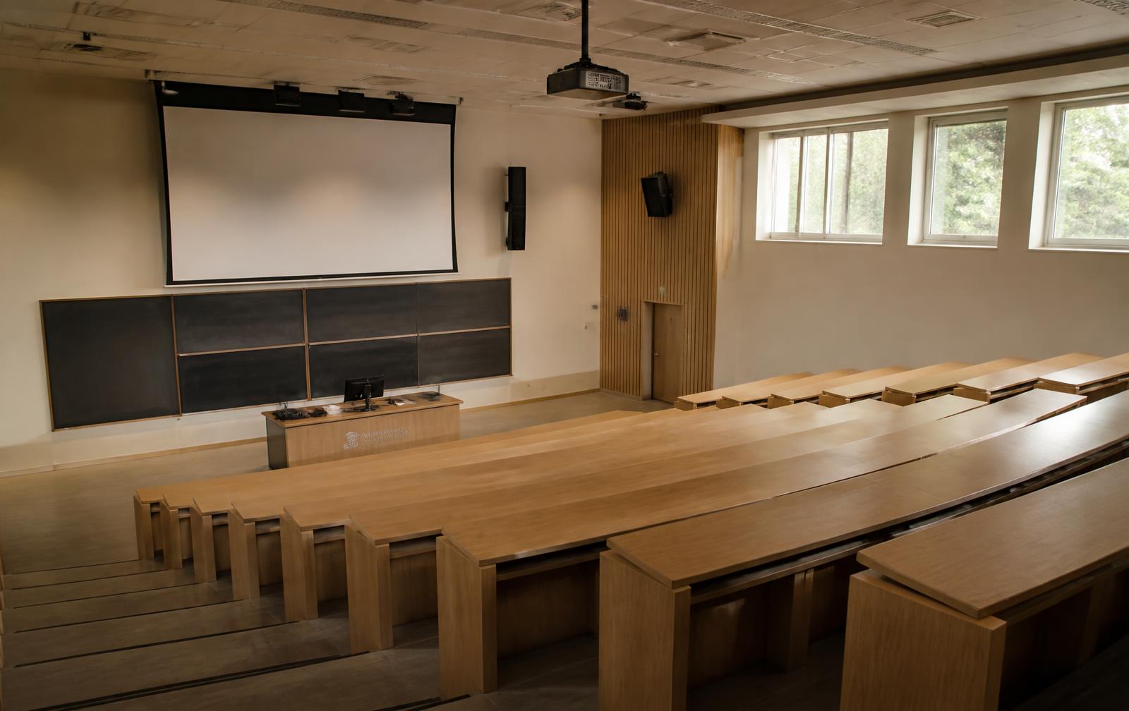 An empty New Zealand university lecture theatre with tiered timber seating and daylight through high windows